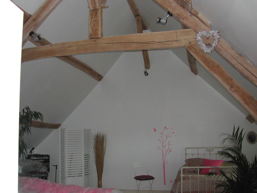 Chambre mansardée chaleureuse avec des poutres en bois apparentes, des murs blancs et un lit avec une parure de lit rose.