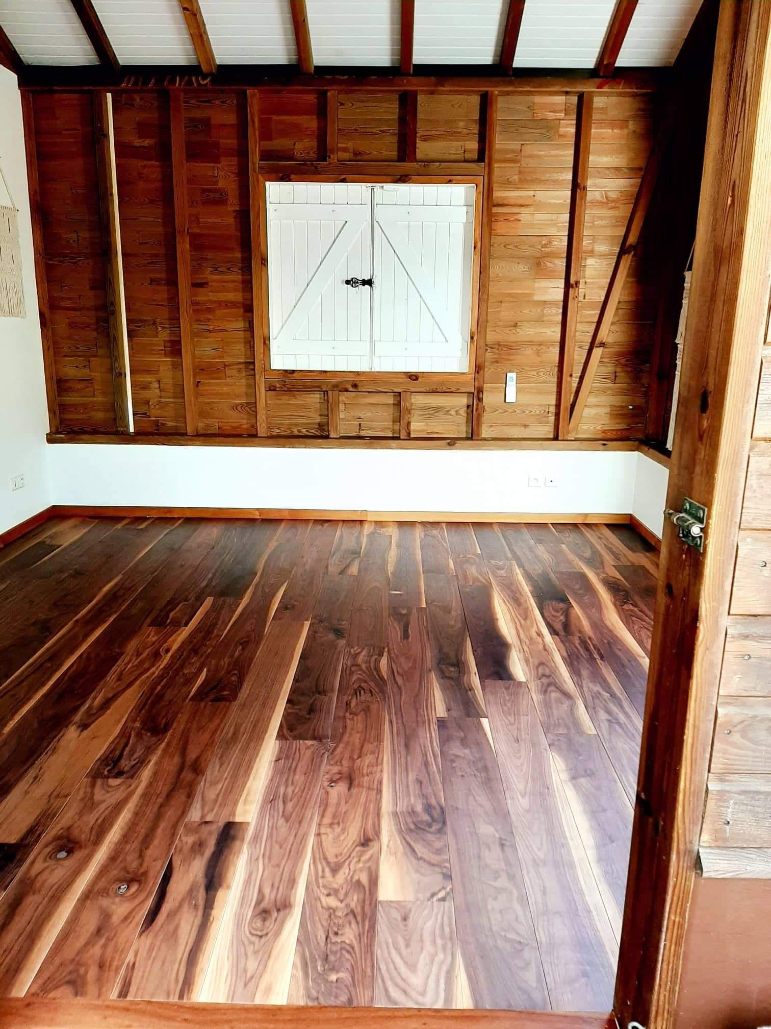 Pièce vide en bois, avec un parquet sombre, des murs lambrissés et une petite fenêtre.