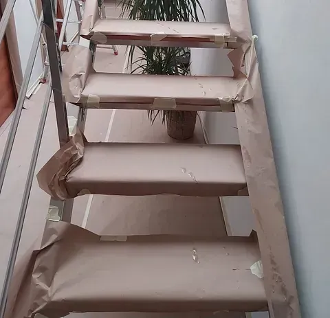 Escalera cubierta con papel marrón para protegerla durante la reforma. Una planta descansa entre los escalones.
