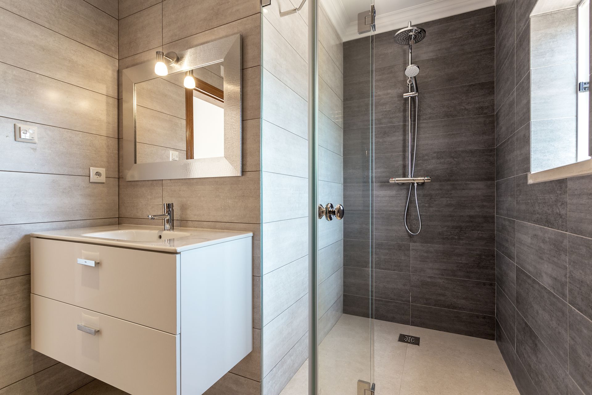 Salle de bains moderne avec meuble-lavabo blanc, miroir et douche à l'italienne aux murs carrelés de gris.