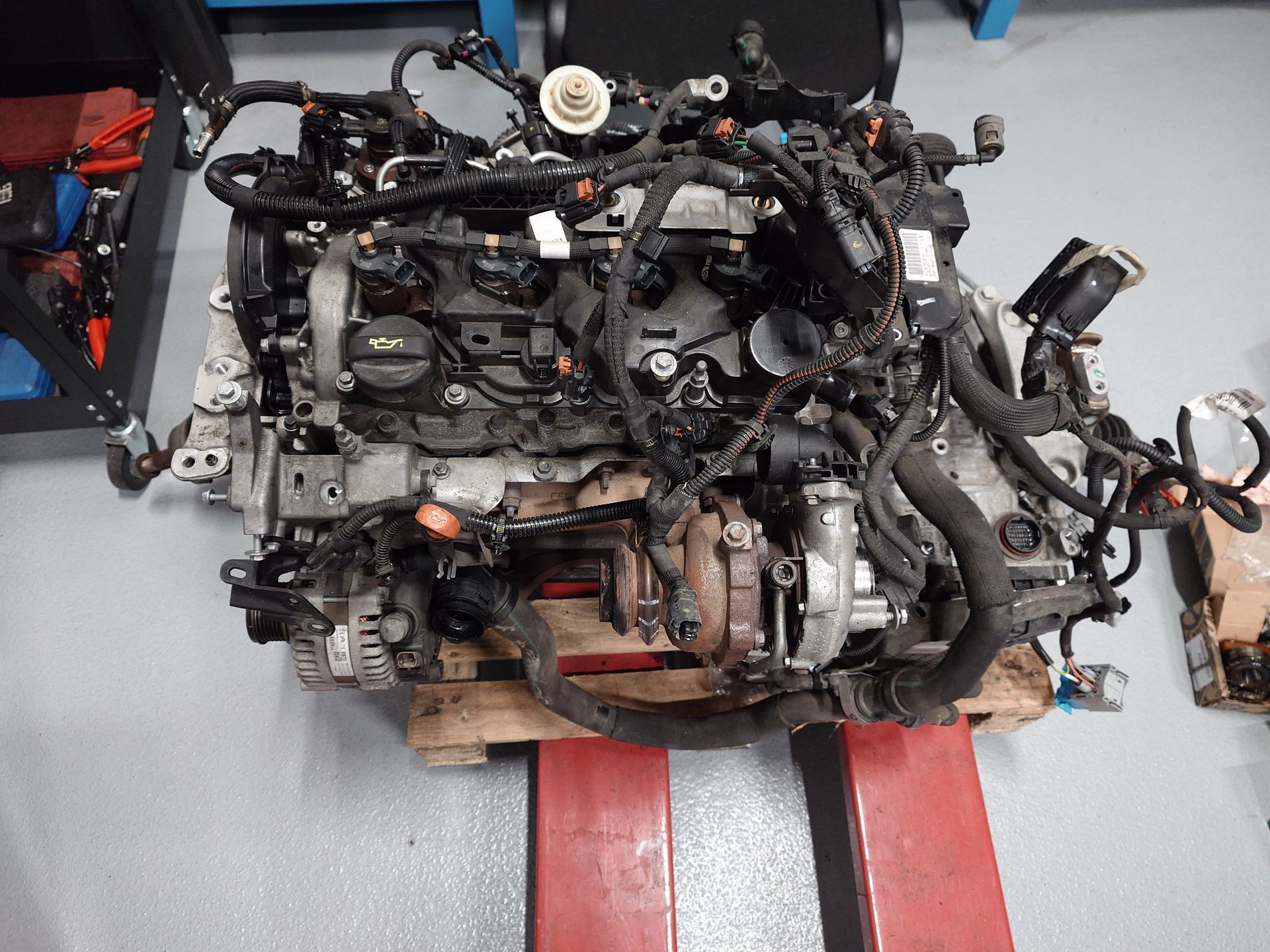 Moteur de voiture posé sur une palette, divers tubes et fils visibles.