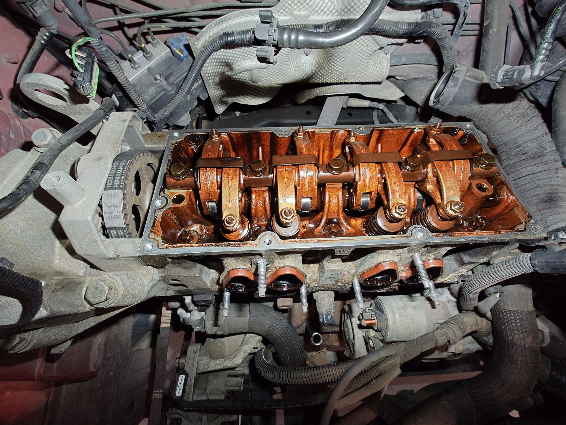 Composants internes du moteur visibles : culbuteurs et train de soupapes recouvert d'huile à l'intérieur d'un compartiment.