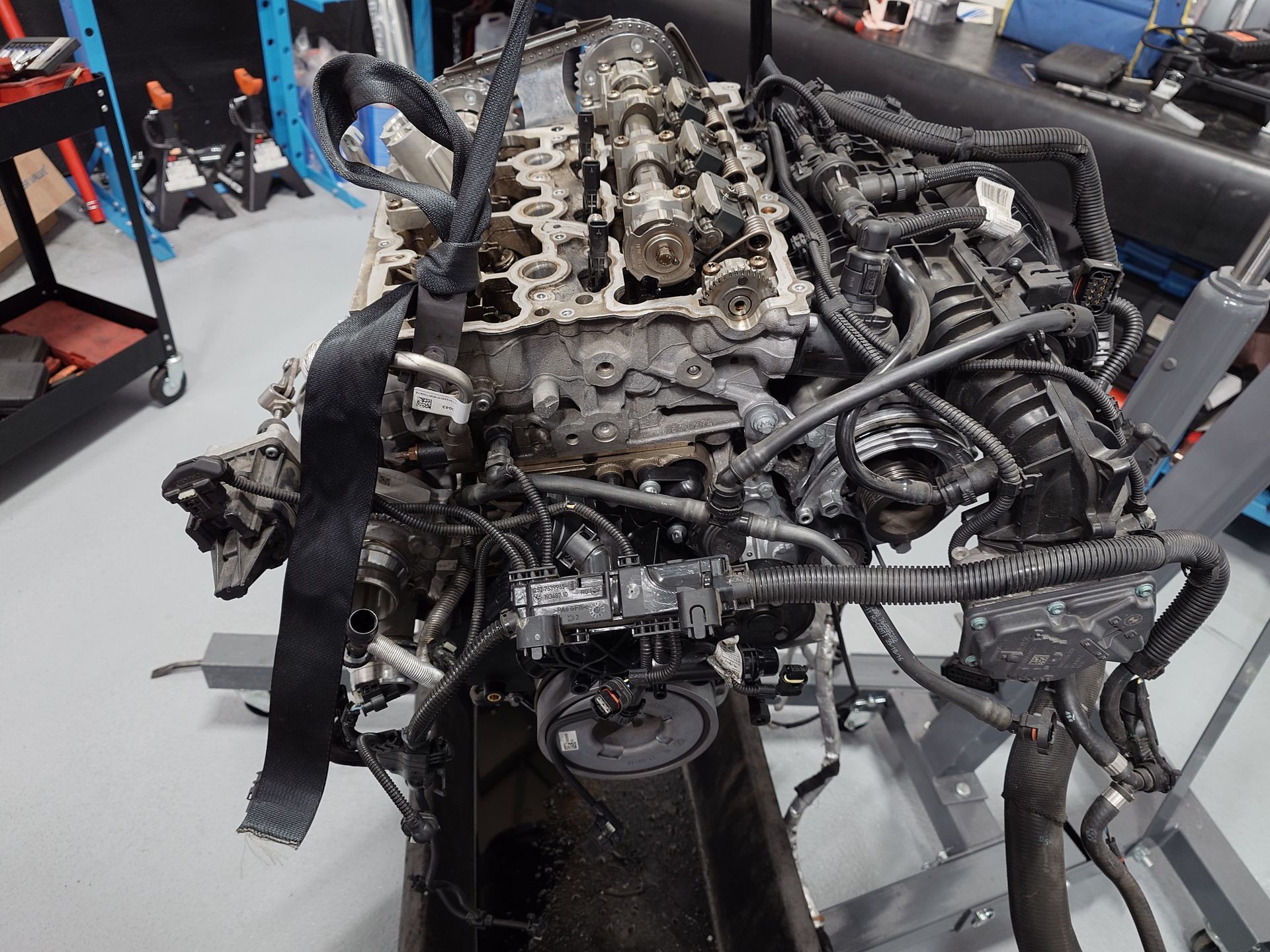 Moteur partiellement démonté sur un support dans un atelier. Câbles noirs, pièces métalliques et mécaniques visibles.