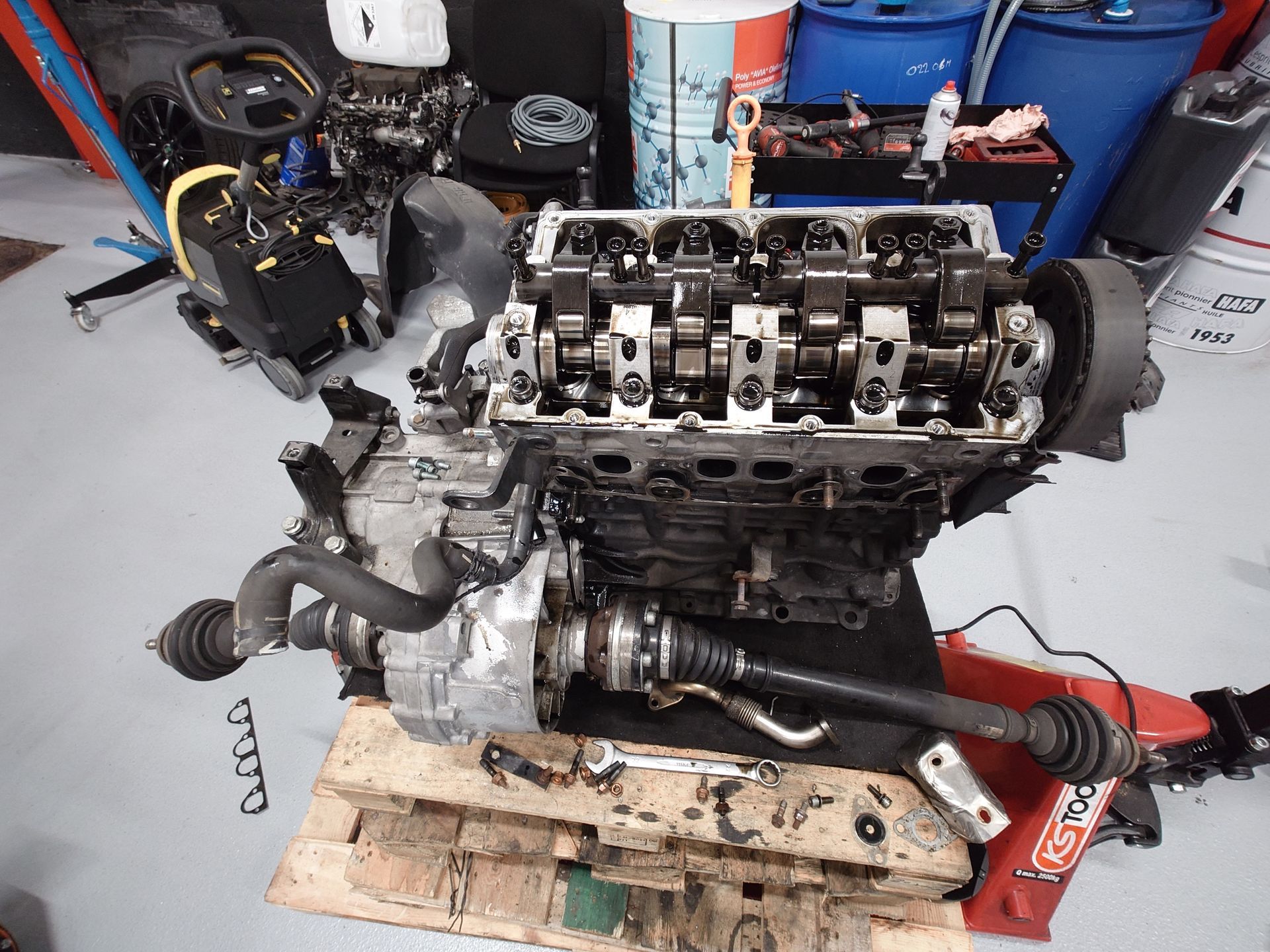 Moteur et transmission sur une palette dans un garage, composants répartis un peu partout.