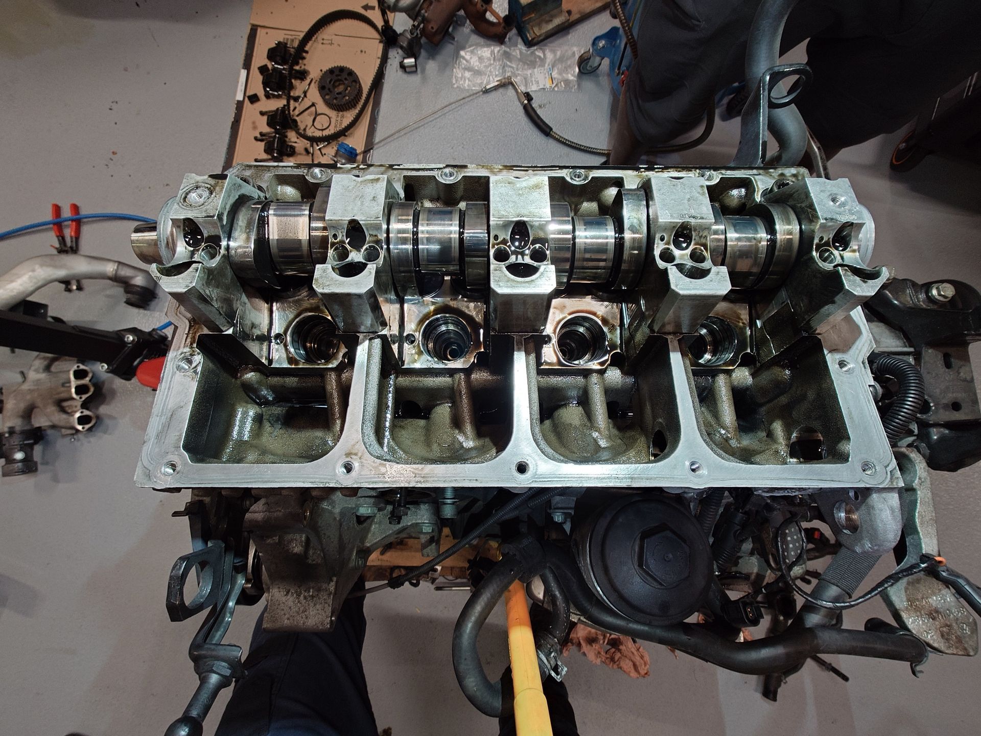 Moteur de voiture démonté avec pistons, arbres à cames et huile visibles, dans un atelier.