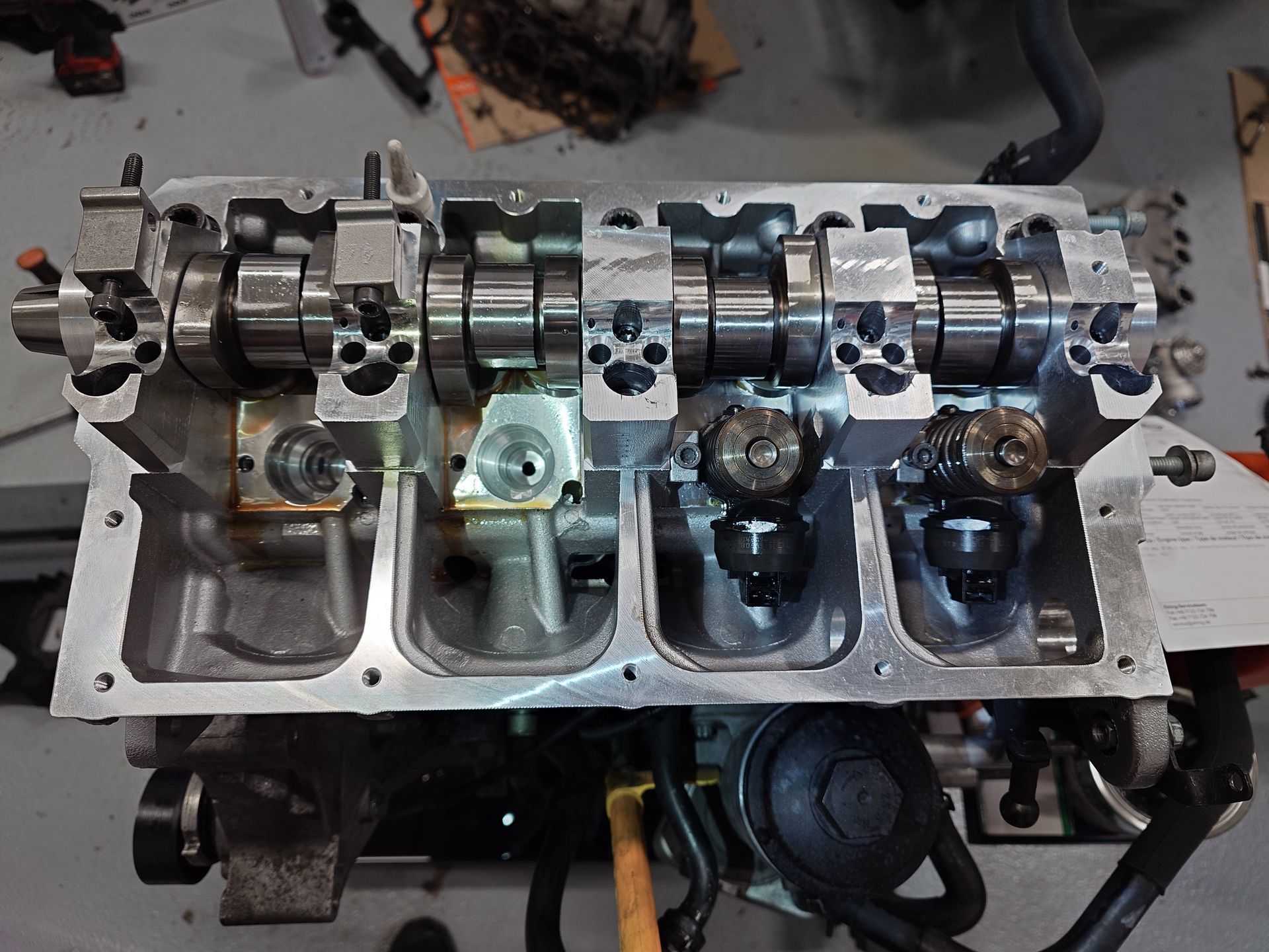 Vue aérienne d'une culasse de moteur avec arbres à cames installés, métal gris et composants sombres visibles.