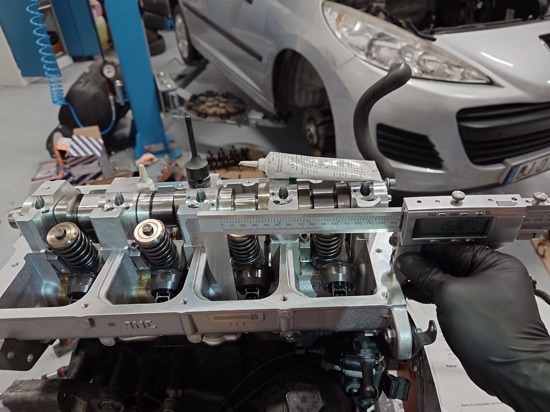 Culasse de moteur de voiture avec un mécanicien la mesurant avec un pied à coulisse numérique dans un garage.