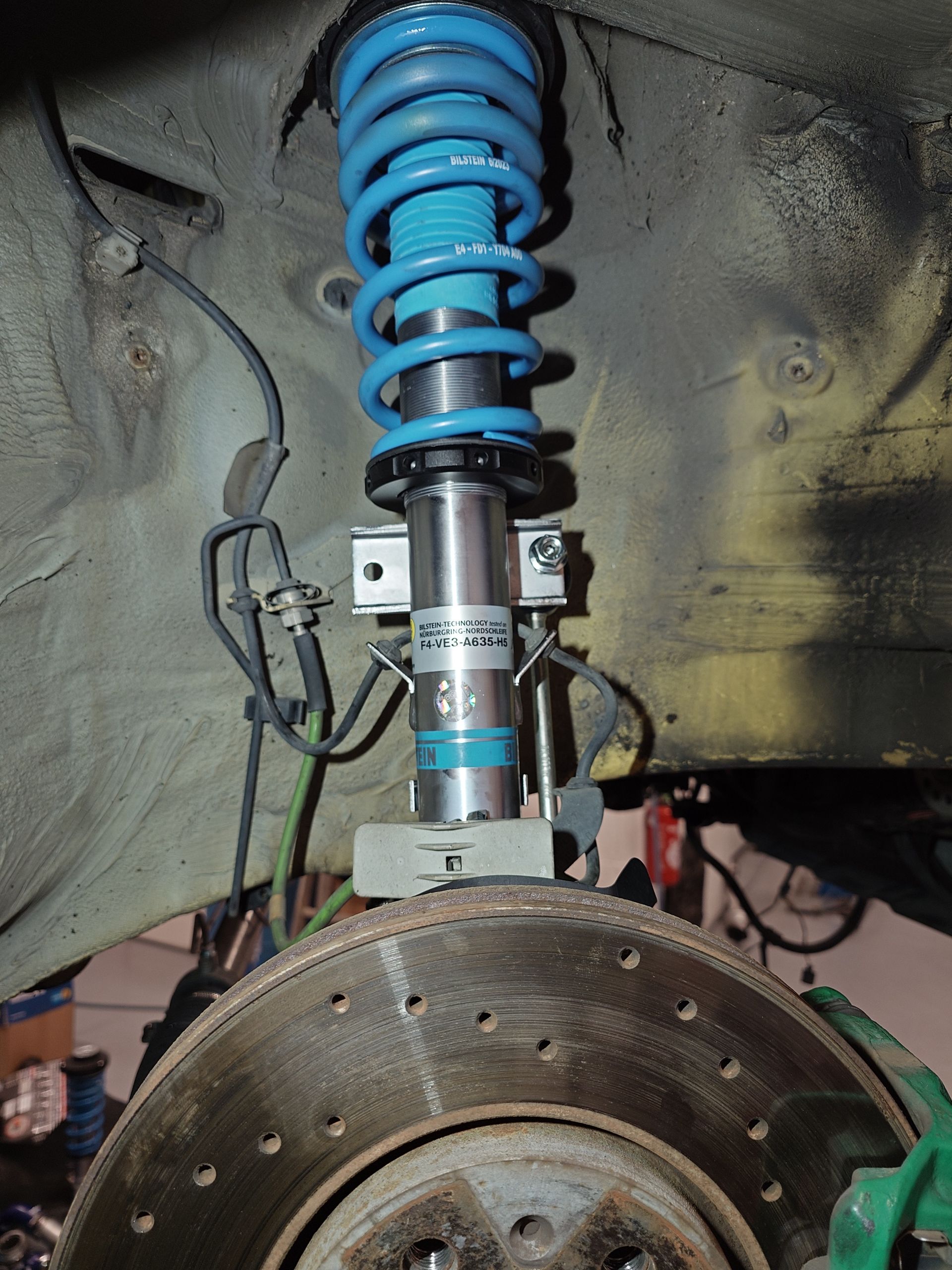 Gros plan du système de suspension de la voiture ; amortisseur à ressorts bleus, rotor de frein et étrier de frein vert.