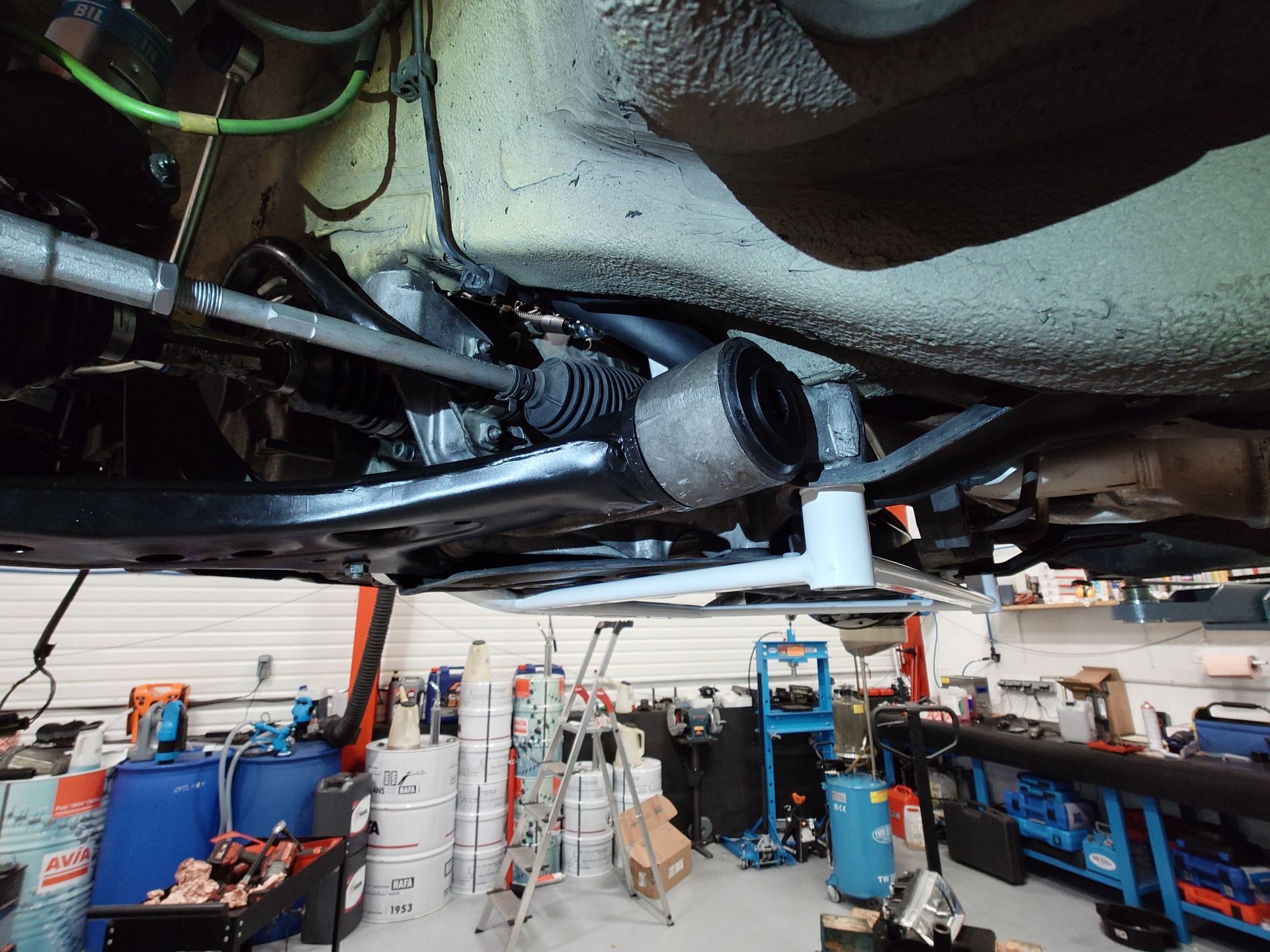 Dessous d'une voiture sur un élévateur dans un atelier, présentant les composants de la suspension et du train de roulement.