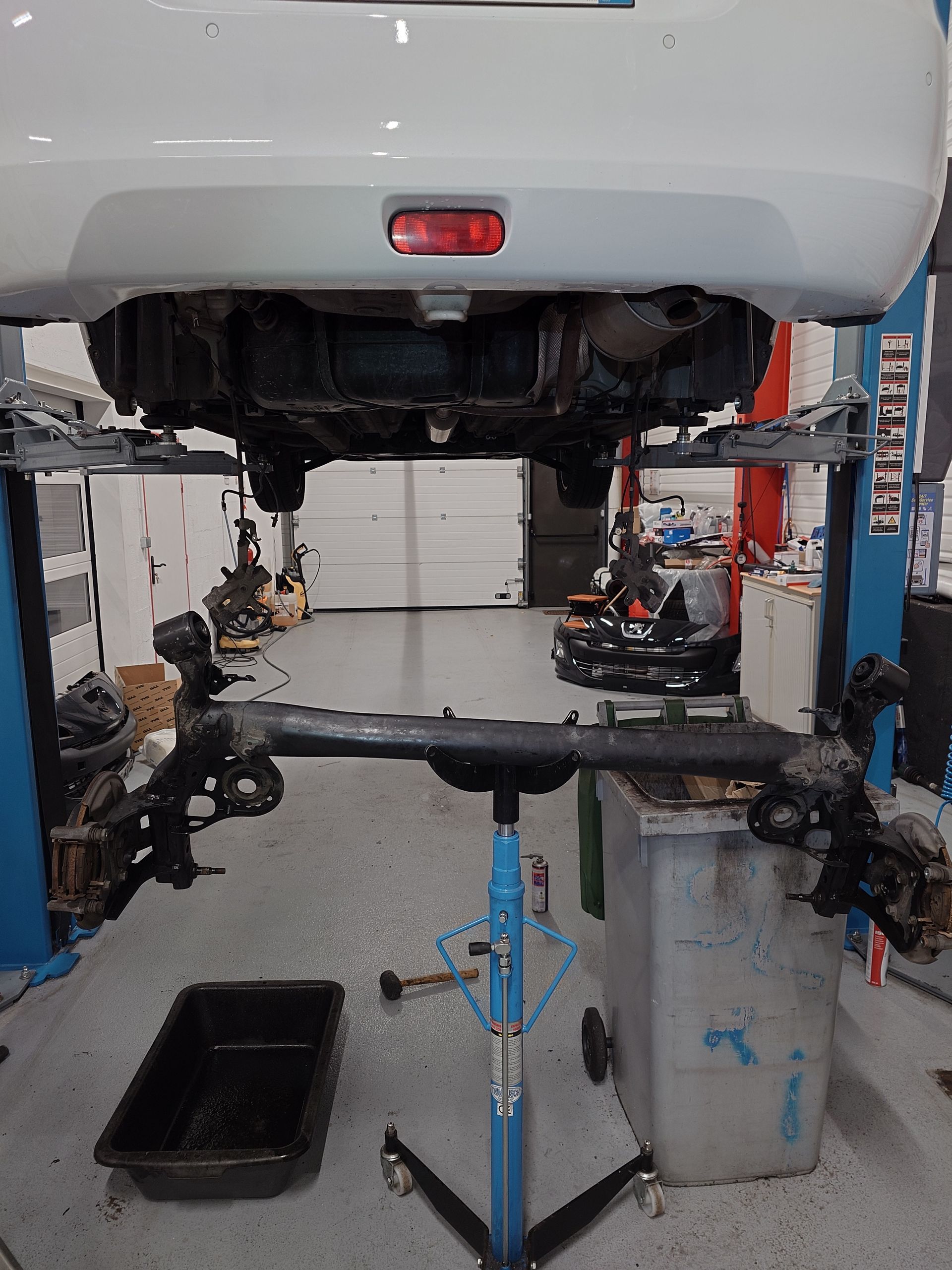 Une voiture sur un élévateur dans un garage, l'essieu arrière retiré, suspendue sur un support à roues.