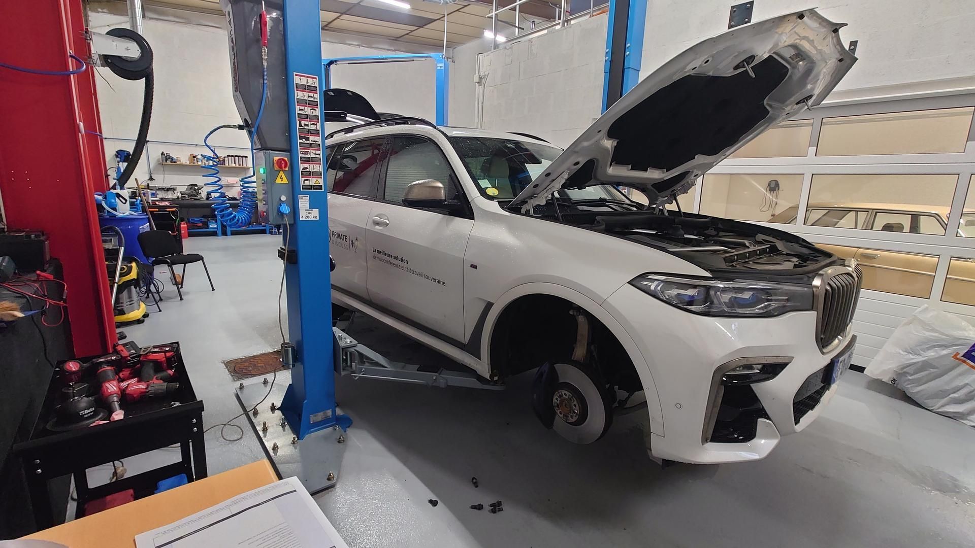 Véhicule blanc sans roue au capot ouvert à l'intérieur d'un garage