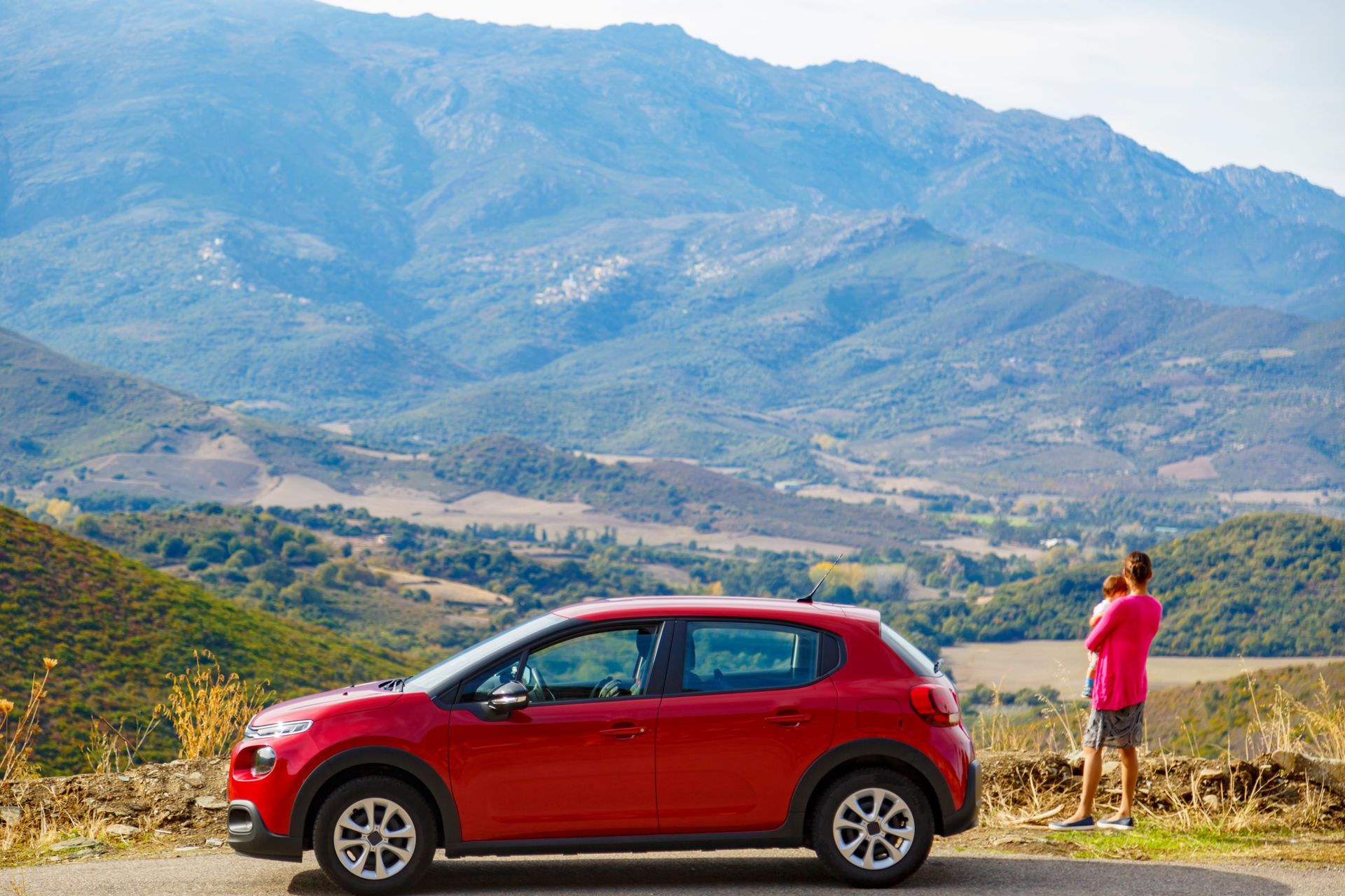 Un père et son enfant derrière une voiture rouge regardent un paysage de montagne