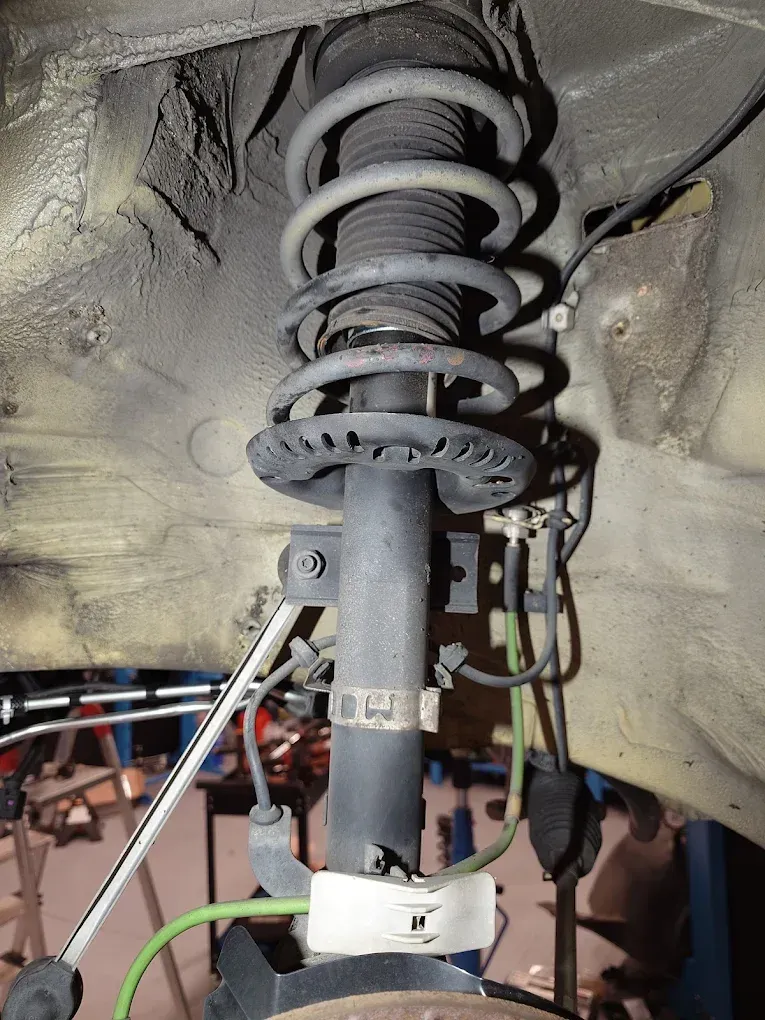 Jambe de force et ressort d'une suspension avant d'une voiture, à l'intérieur d'un passage de roue, avec les câbles et la saleté autour