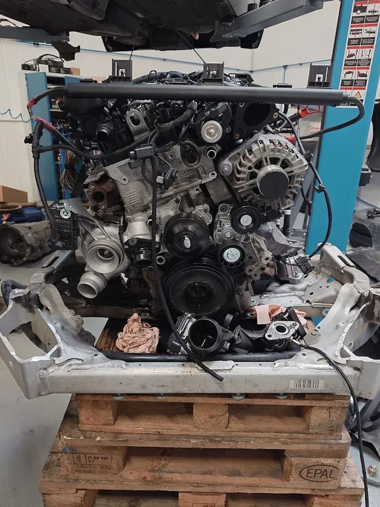 Moteur de voiture partiellement démonté sur une palette dans un atelier, avec courroies et poulies apparentes