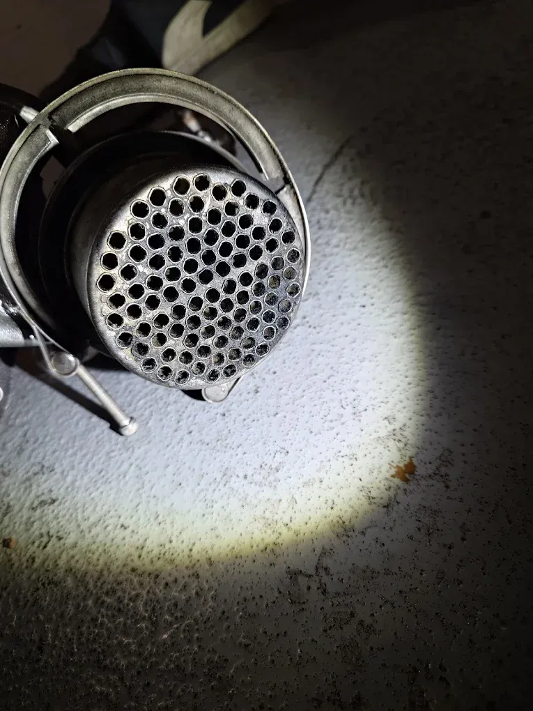 Gros plan d'un tuyau d'échappement métallique à extrémité perforée, éclairé par une lampe torche, sur une surface sombre