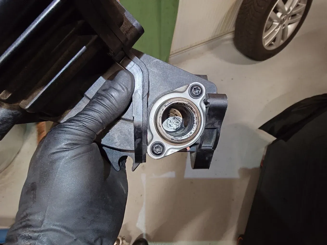 Main gantée tenant une pièce métallique automobile près d'une roue de voiture, dans un garage