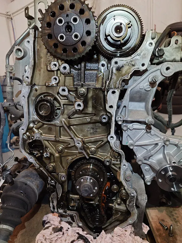 Face avant d'un moteur de voiture démonté, avec pignons de distribution et pièces métalliques tachées d'huile