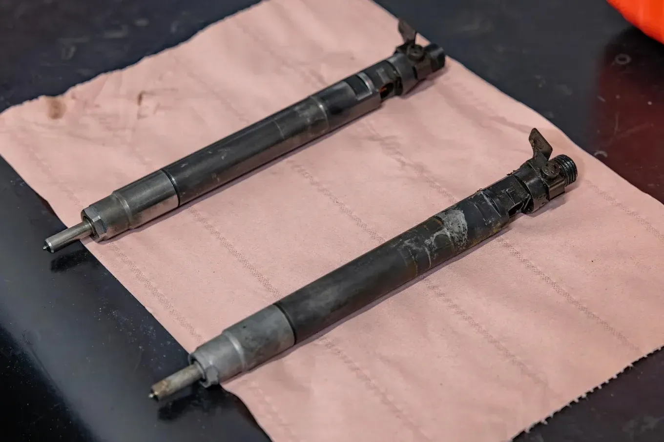 Deux injecteurs noirs disposés parallèlement sur un tissu rose