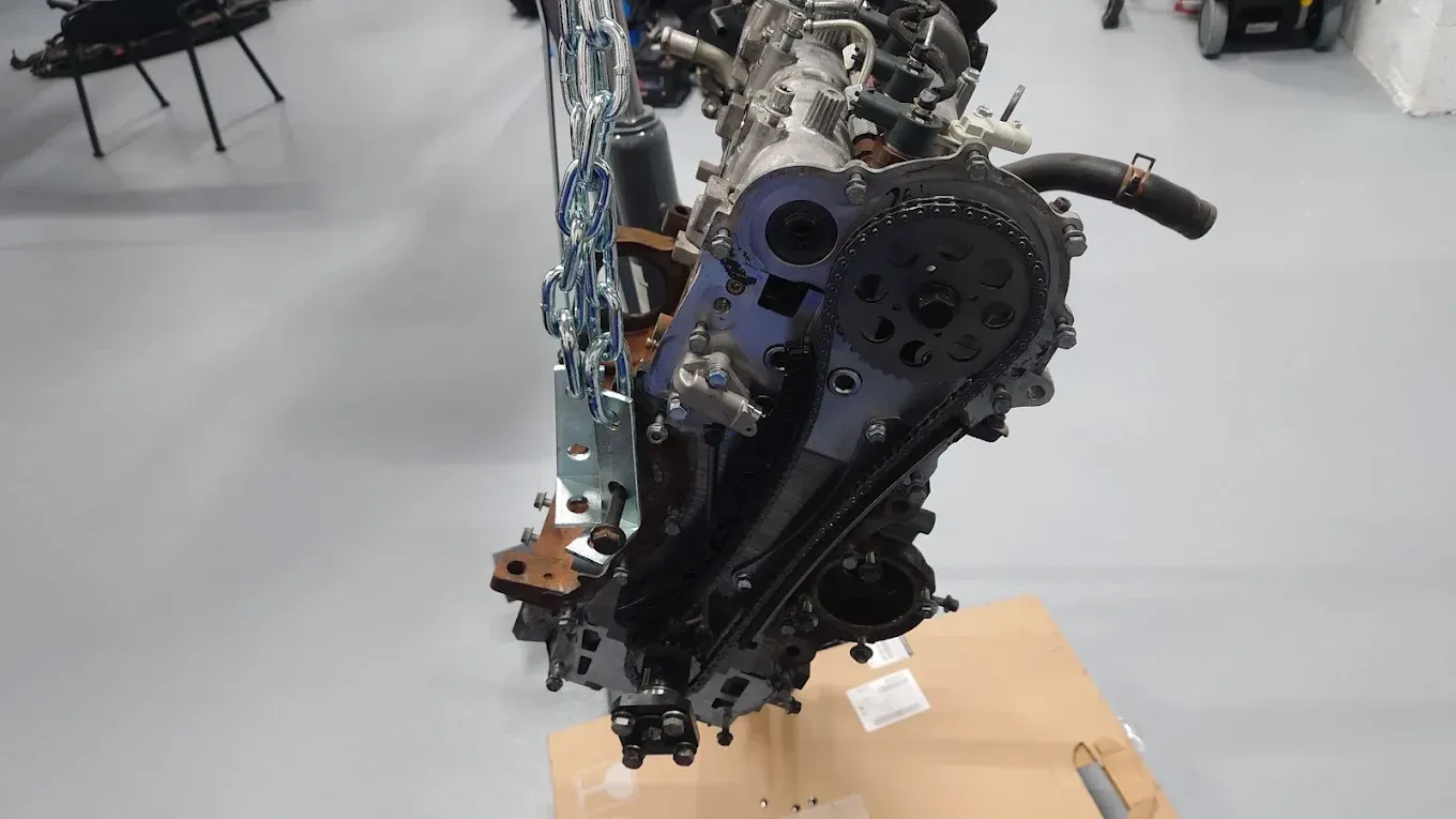Moteur de voiture démonté, exposé sur un support dans un atelier, avec des pièces métalliques et des tuyaux apparents