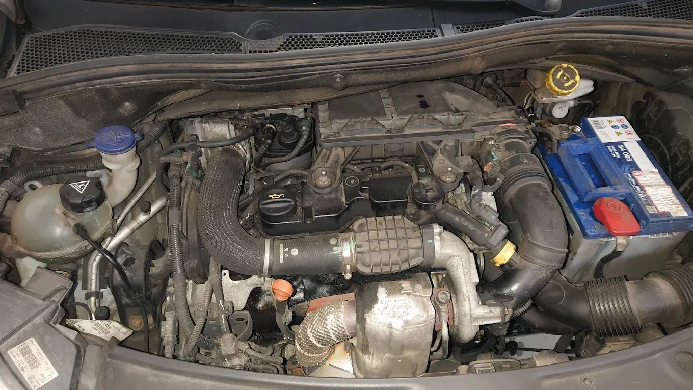 Voiture grise avec le capot ouvert, montrant le compartiment moteur avec batterie, durites et composants