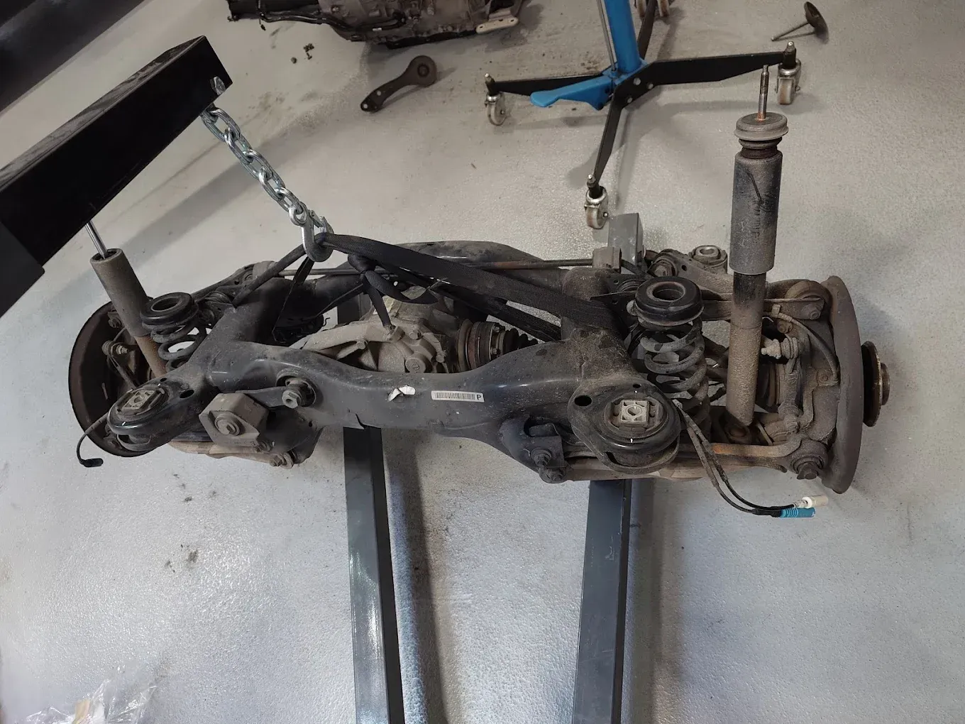 Suspension et essieu d'une voiture détachés, posés sur un sol en béton dans un garage