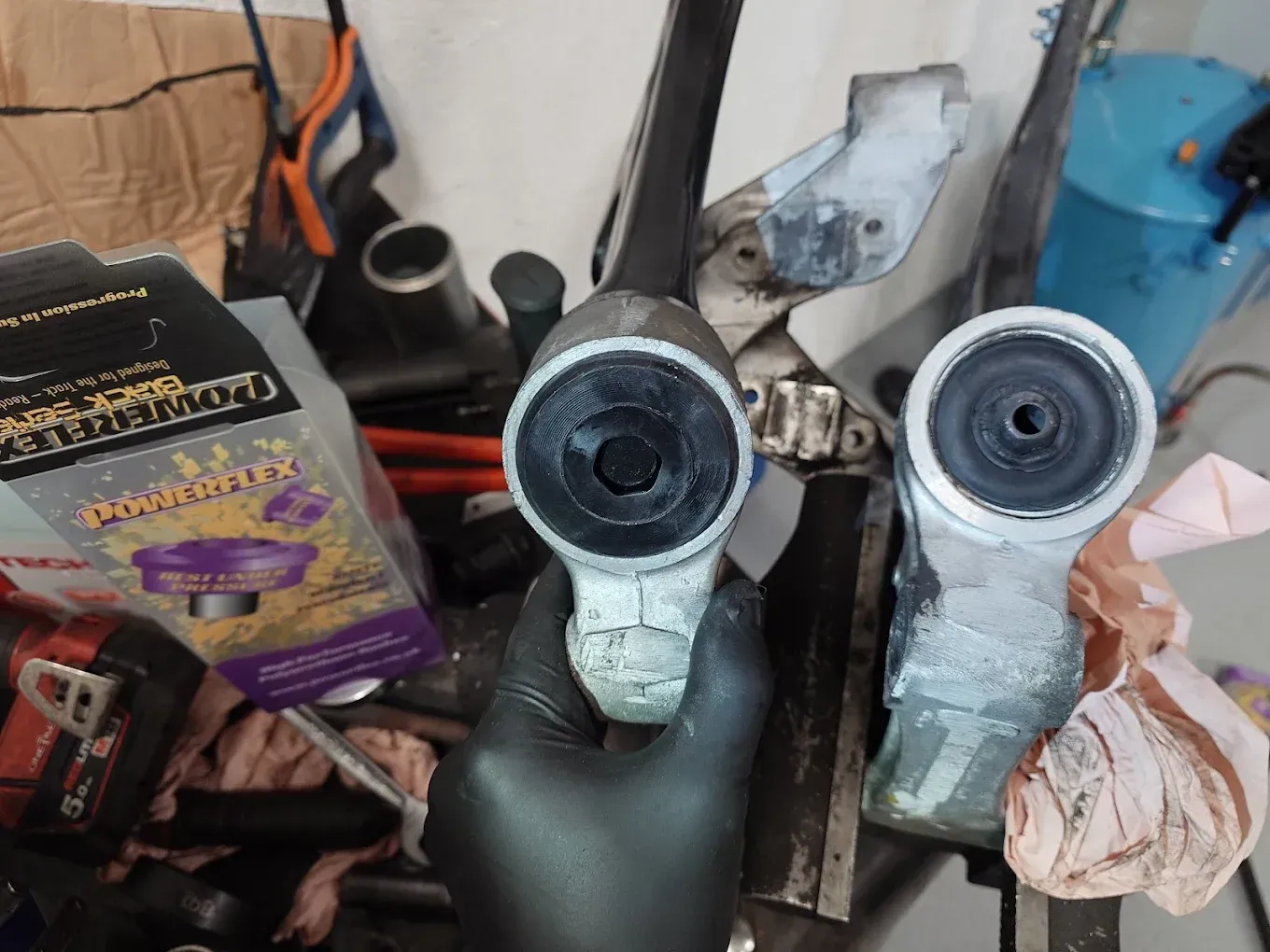 Deux pièces mécaniques tenues dans une main gantée, dans un atelier encombré, avec des outils et des boîtes à proximité