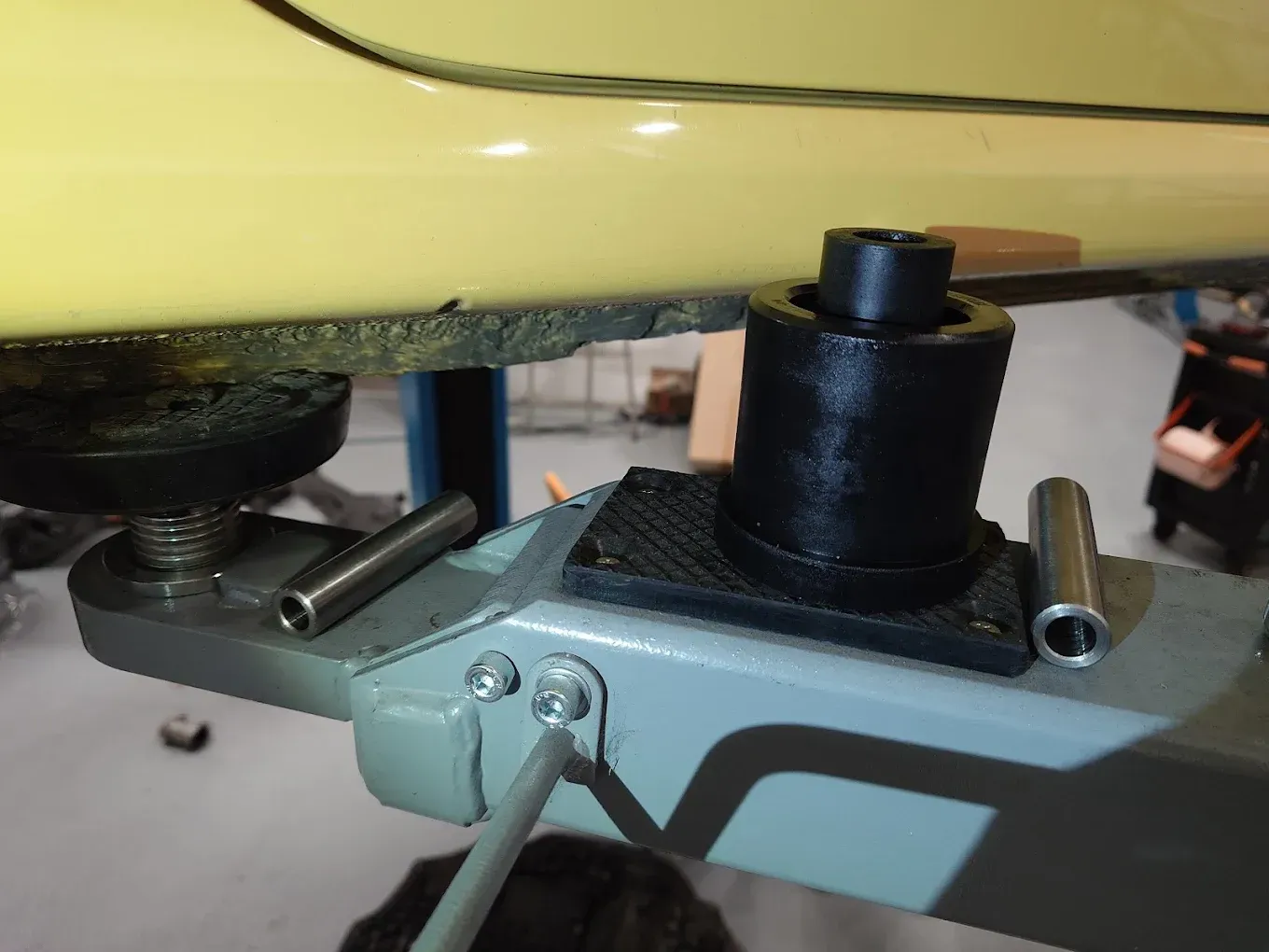 Gros plan le bas de caisse d'une voiture jaune, montée sur un pont élévateur