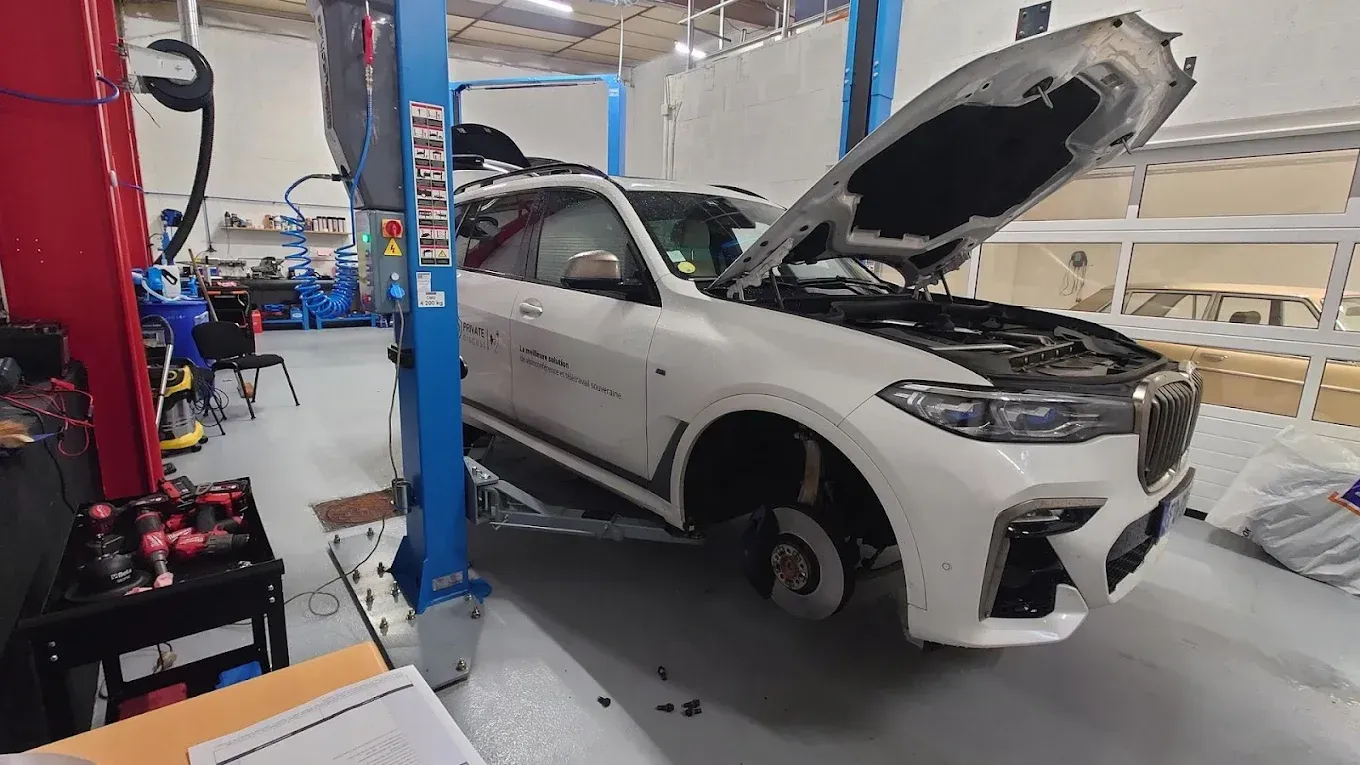 SUV blanc sur un pont élévateur, dans un garage, capot ouvert et roue avant démontée