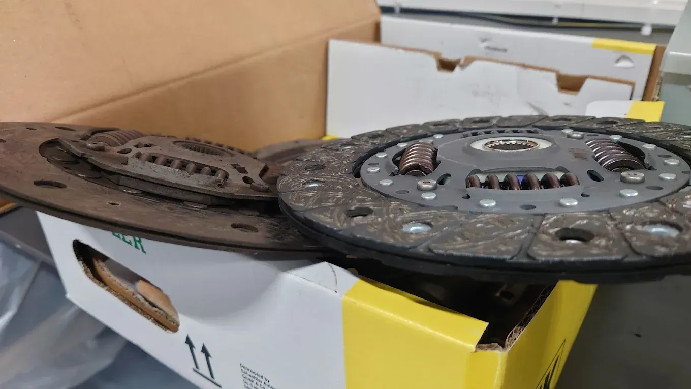 Deux disques d'embrayage reposent sur une boîte, celui de gauche est usé, celui de droite est neuf