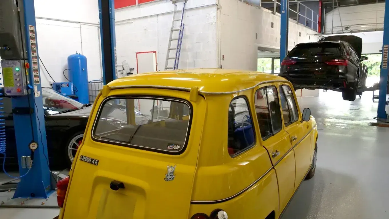 Voiture jaune ancienne dans un atelier, avec une voiture noire surélevée en arrière-plan