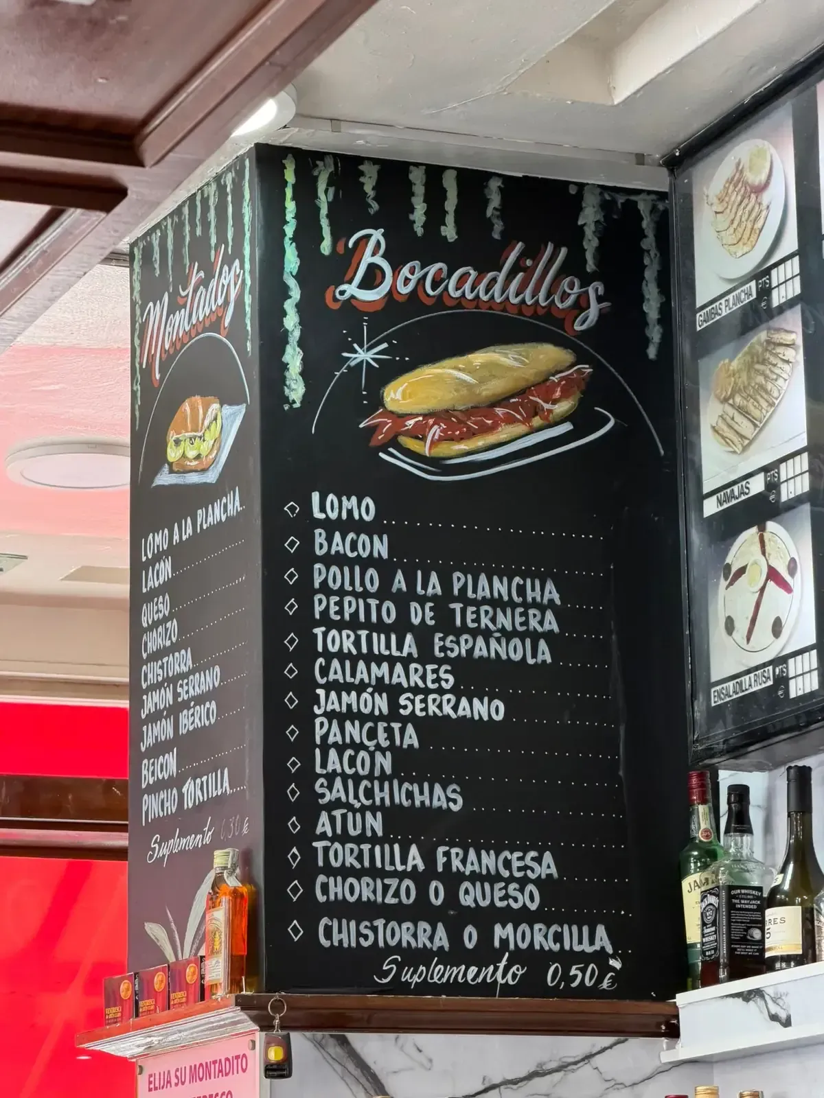 Menú escrito en una pizarra negra con la lista de sándwiches y rellenos en portugués, y una foto de un sándwich en la parte superior.