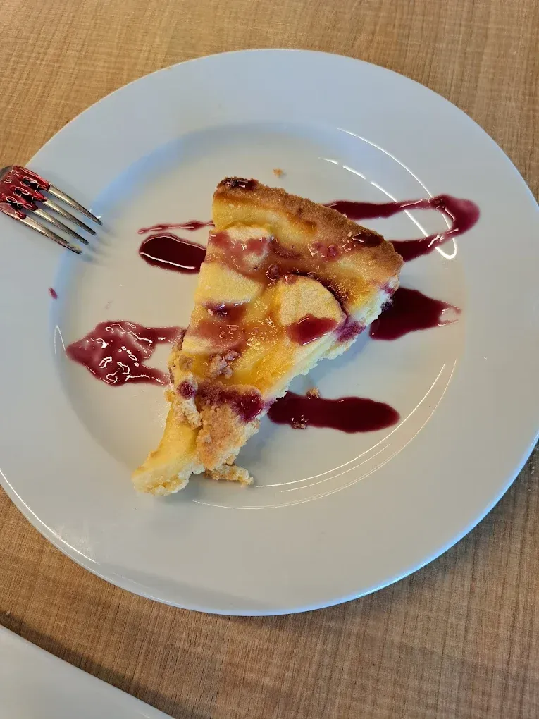 Una porción de tarta de queso con salsa de frutos rojos en un plato blanco con un tenedor sobre una mesa.