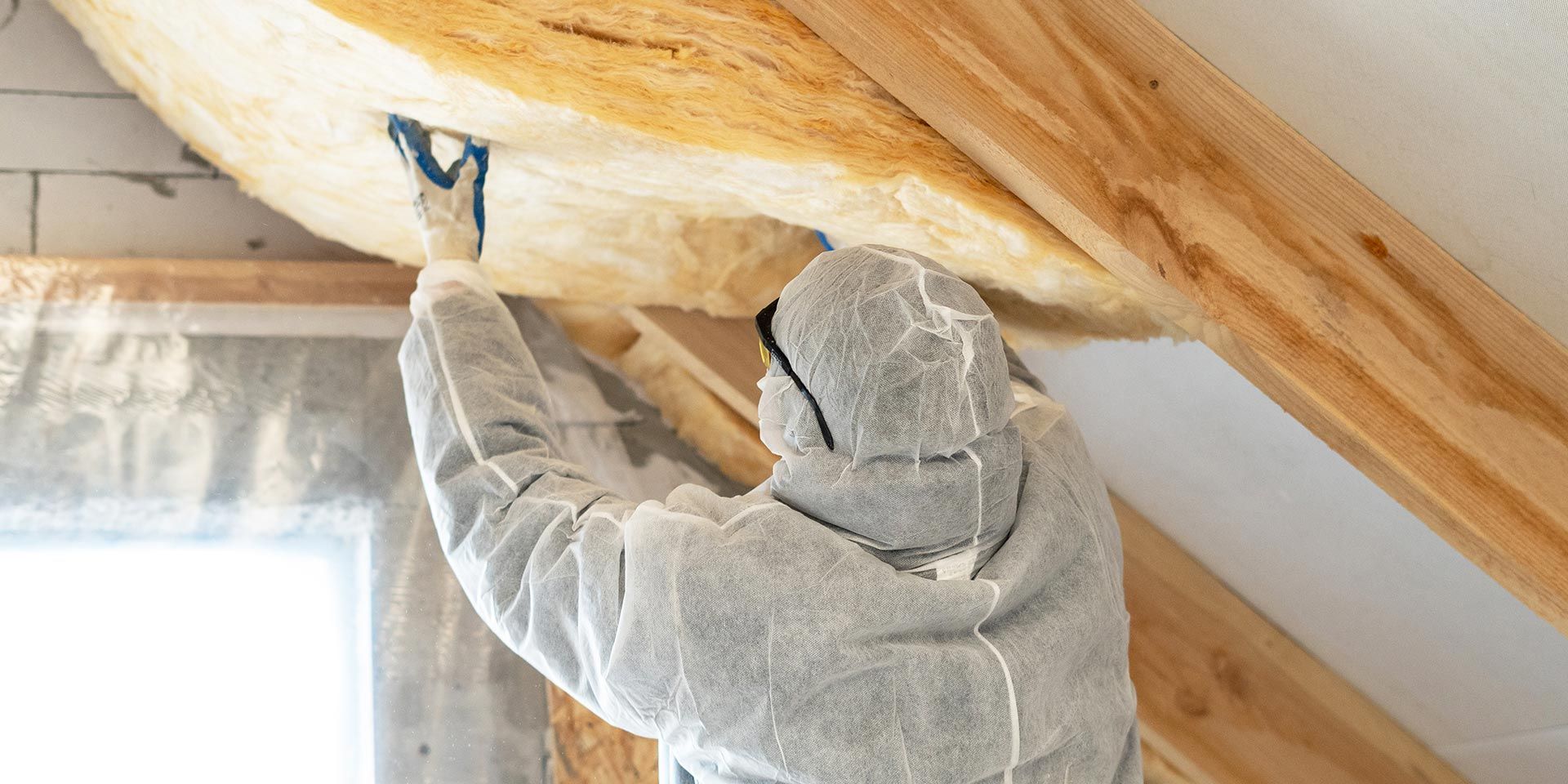 Homme en combinaison de protection qui pose des panneaux de laine de verre sous les combles