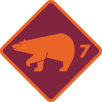 Ein orangefarbener Bär geht nach rechts; darin befindet sich die Zahl 7 in einer kastanienbraunen und orangefarbenen Raute.