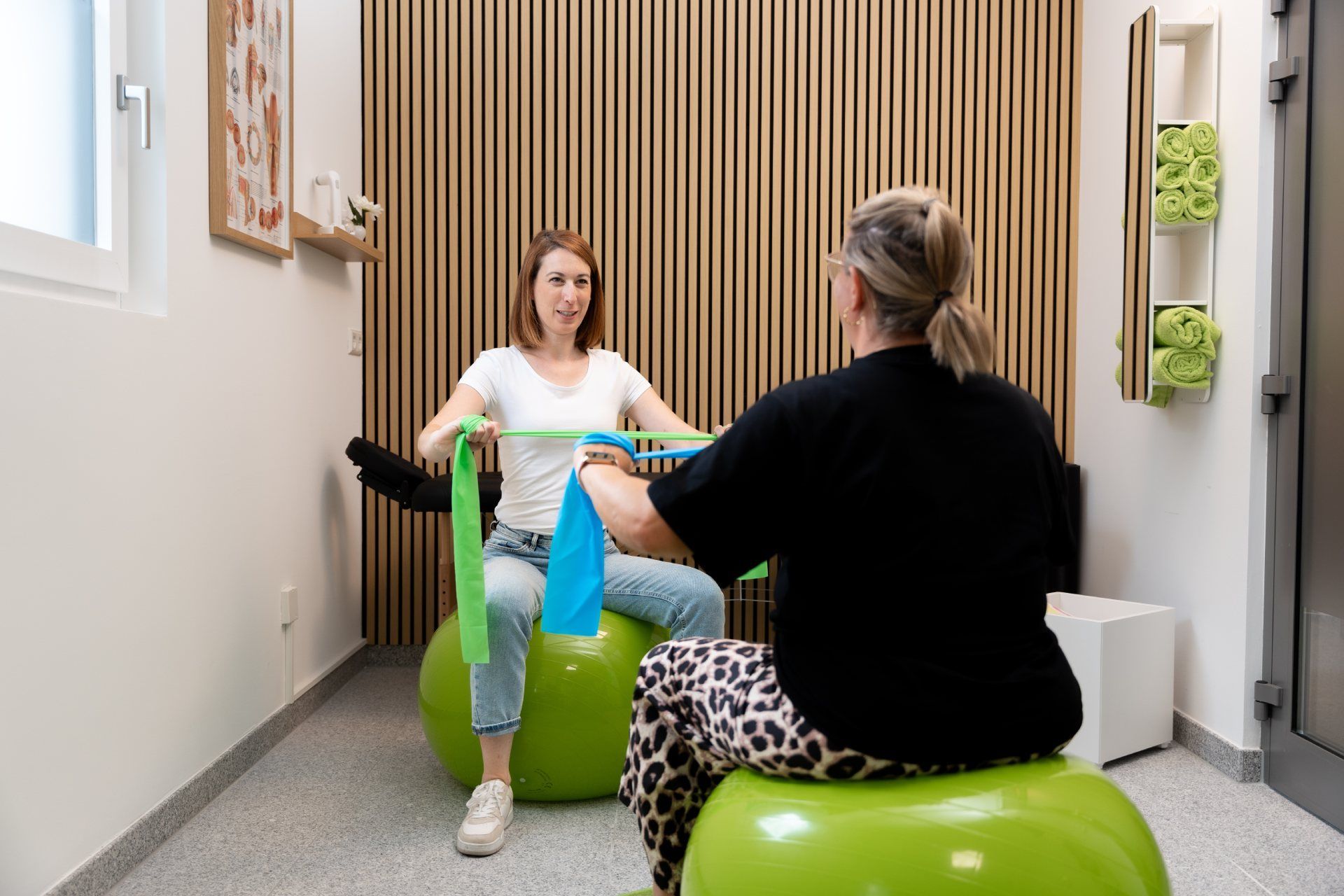 Zwei Personen sitzen in einem Therapieraum auf grünen Gymnastikbällen, einander gegenüber