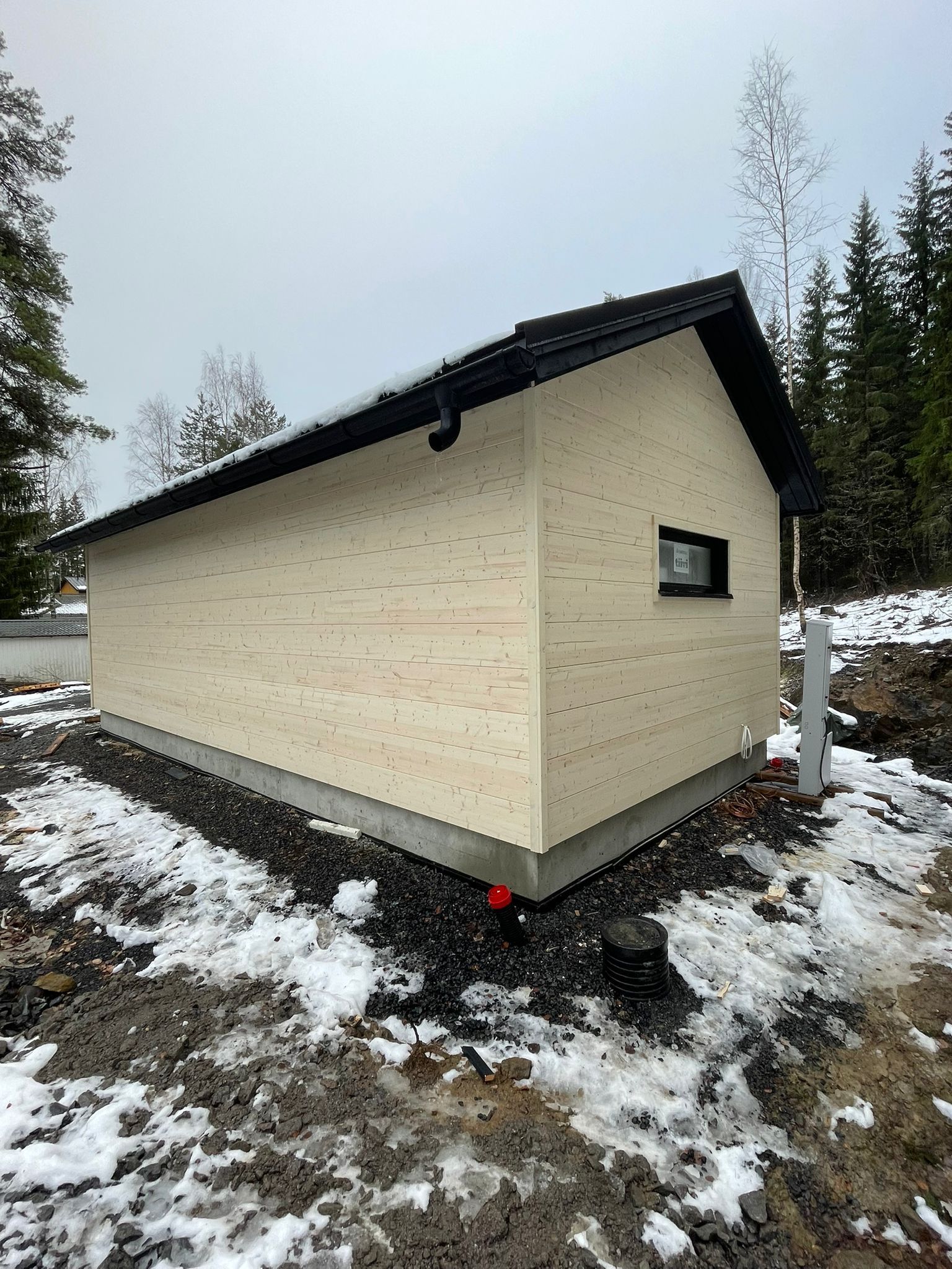 Pieni beigenvärinen vaja, jossa on tumma katto, lumisella metsäalueella
