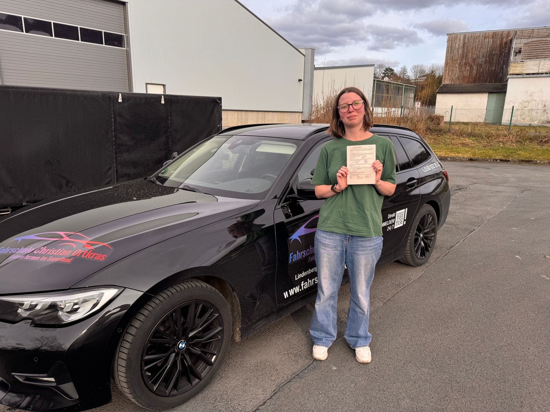Eine Frau steht mit einem Zertifikat vor einem schwarzen Auto.
