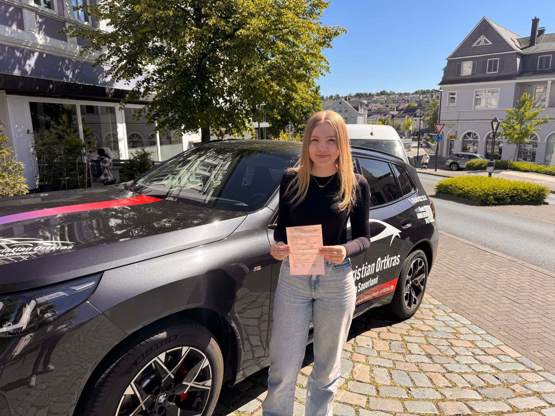 Eine Frau steht vor einem Auto und hält ein Nummernschild hoch.