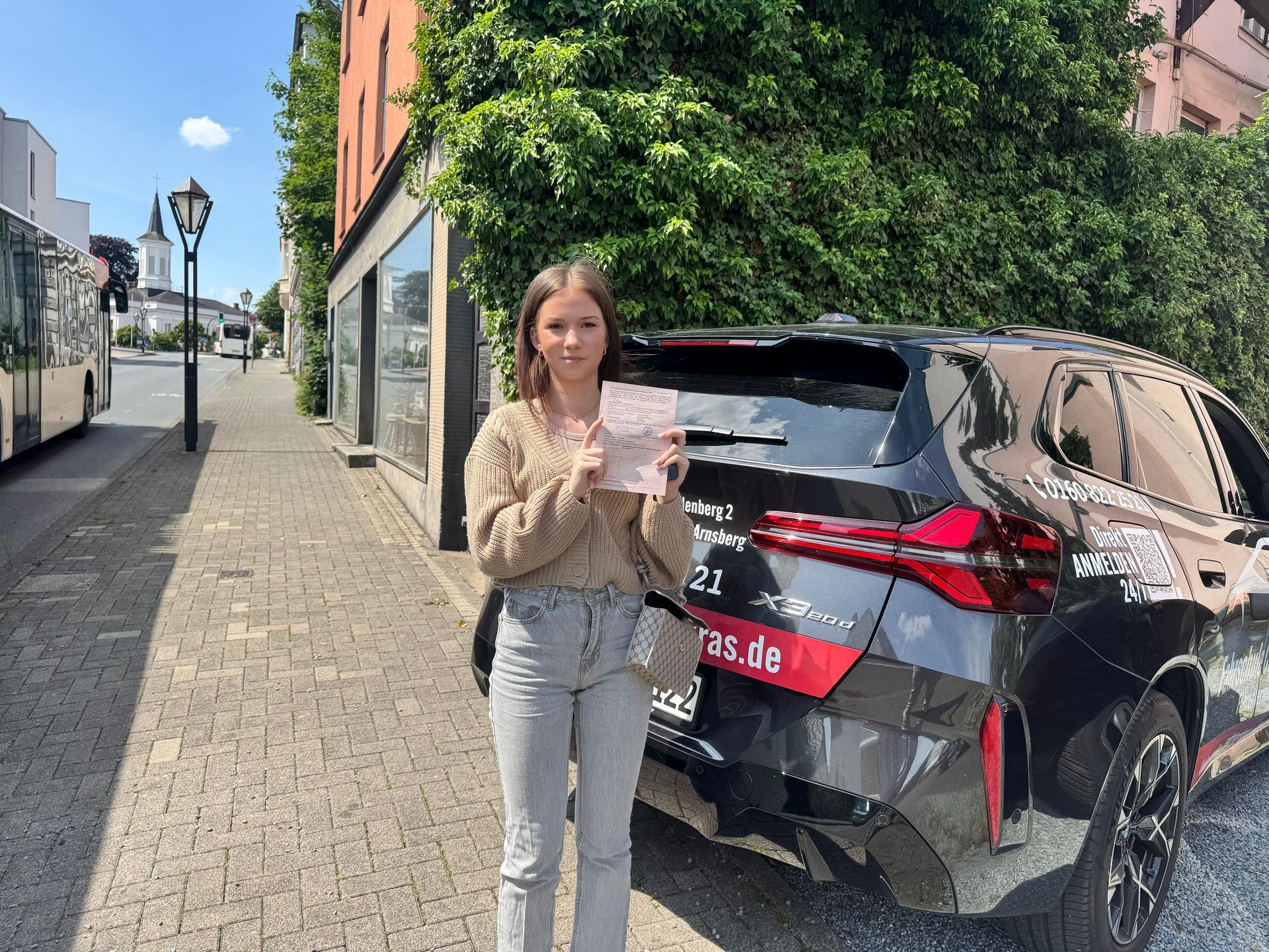 Eine Frau steht vor einem Auto und hält ein Nummernschild hoch.