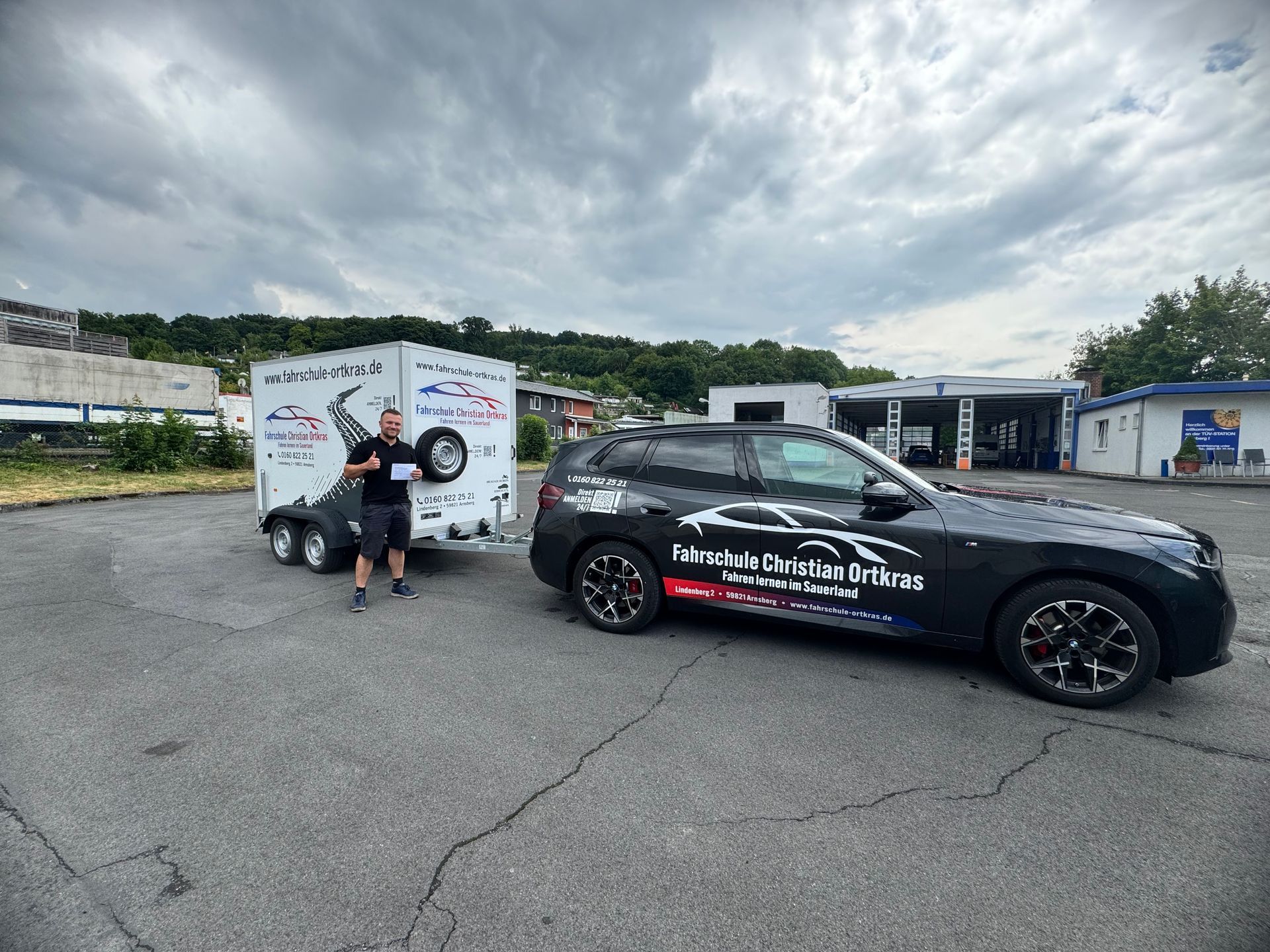 Ein Mann steht auf einem Parkplatz neben einem Auto mit Anhänger.