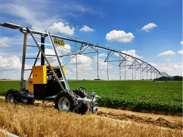 Un tractor avanza por un campo con un sistema de riego al fondo.