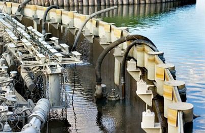 Una fila de tuberías están conectadas a una pared al lado de un cuerpo de agua.