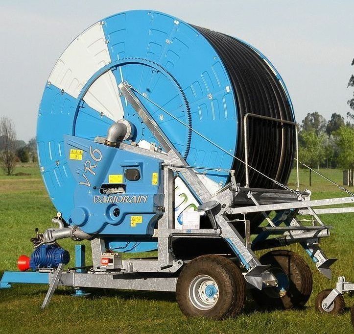 Una gran máquina de riego azul y blanca se encuentra en un campo de hierba.