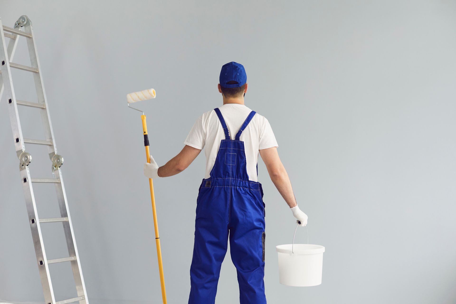 Un hombre está pintando una pared con un rodillo de pintura y un balde.