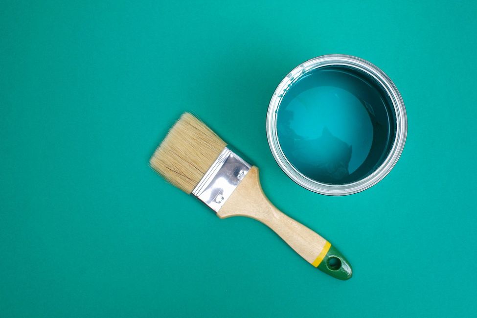 Un pincel y una lata de pintura azul sobre un fondo verde.