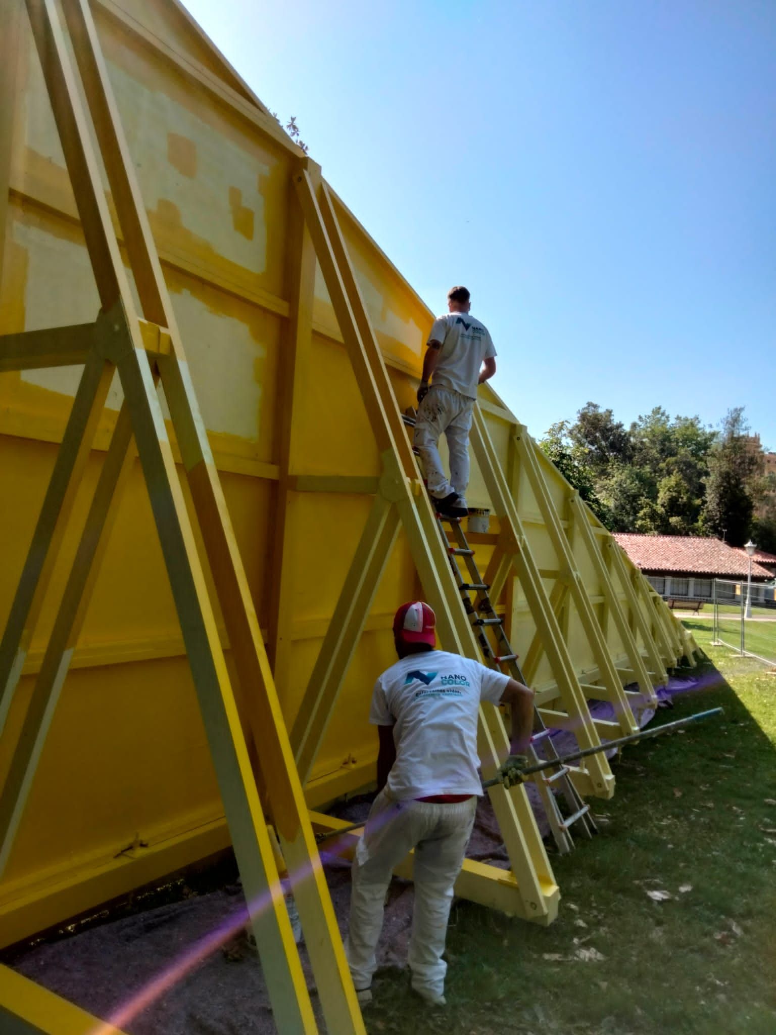 Dos hombres están pintando una gran estructura amarilla.