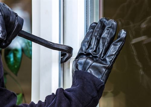 Ein Einbrecher schlägt mit einem Schraubenschlüssel ein Fenster ein.