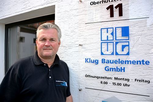 Ein Mann steht vor einem Schild mit der Aufschrift „Klug Bauelemente GmbH“.