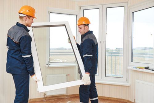 Zwei Männer bauen in einem Zimmer ein Fenster ein.