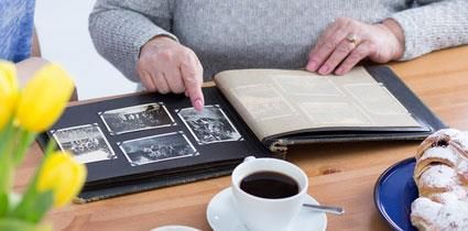 Eine Frau sitzt an einem Tisch und schaut sich ein Fotoalbum an.